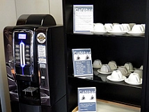 Der schwarze Getränkeautomat bietet verschiedene Kaffeesorten und andere Heißgetränke an. Im Regal daneben befinden sich Tassen und Espressotassen aus Porzellan. © Universitätsstadt Marburg