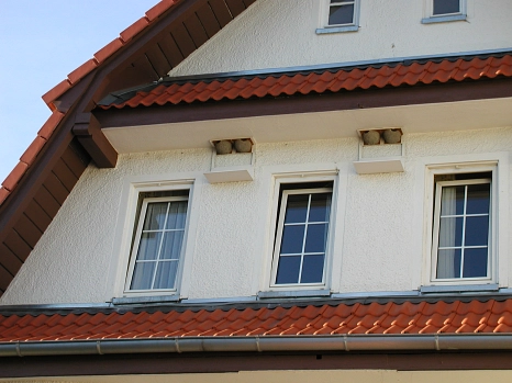 Hausfassade mit tonfarbigen Mehlschwalbennisthilfen und der Fassade farblich angepasste Kotbretter