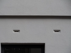 Zwei schmale waagerechte Einflugritzen für Fledermäuse in einer Hausfassade (Nahaufnahme).