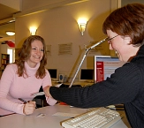 Eine lachende Mitarbeiterin der Stadtbücherei überreicht einer freundlichen Kundin an der Anmeldung Unterlagen. © Universitätsstadt Marburg